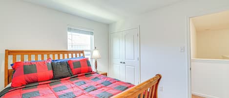 A bedroom with a wooden bed, a window with blinds, a white door, and a carpeted floor.