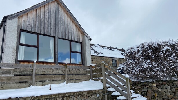 Un edificio rústico de madera con amplias ventanas y una escalera de piedra que conduce a una puerta de madera.