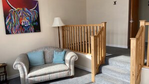 Una sala de estar con un sofá estampado, una escalera de madera y un cuadro de colores en la pared.