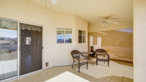 A covered patio with a sliding glass door, two wicker chairs, a small round table, and a ceiling fan. - Hike, Boat, Golf & Unwind: Lake Havasu City Home! (Lake Havasu City)