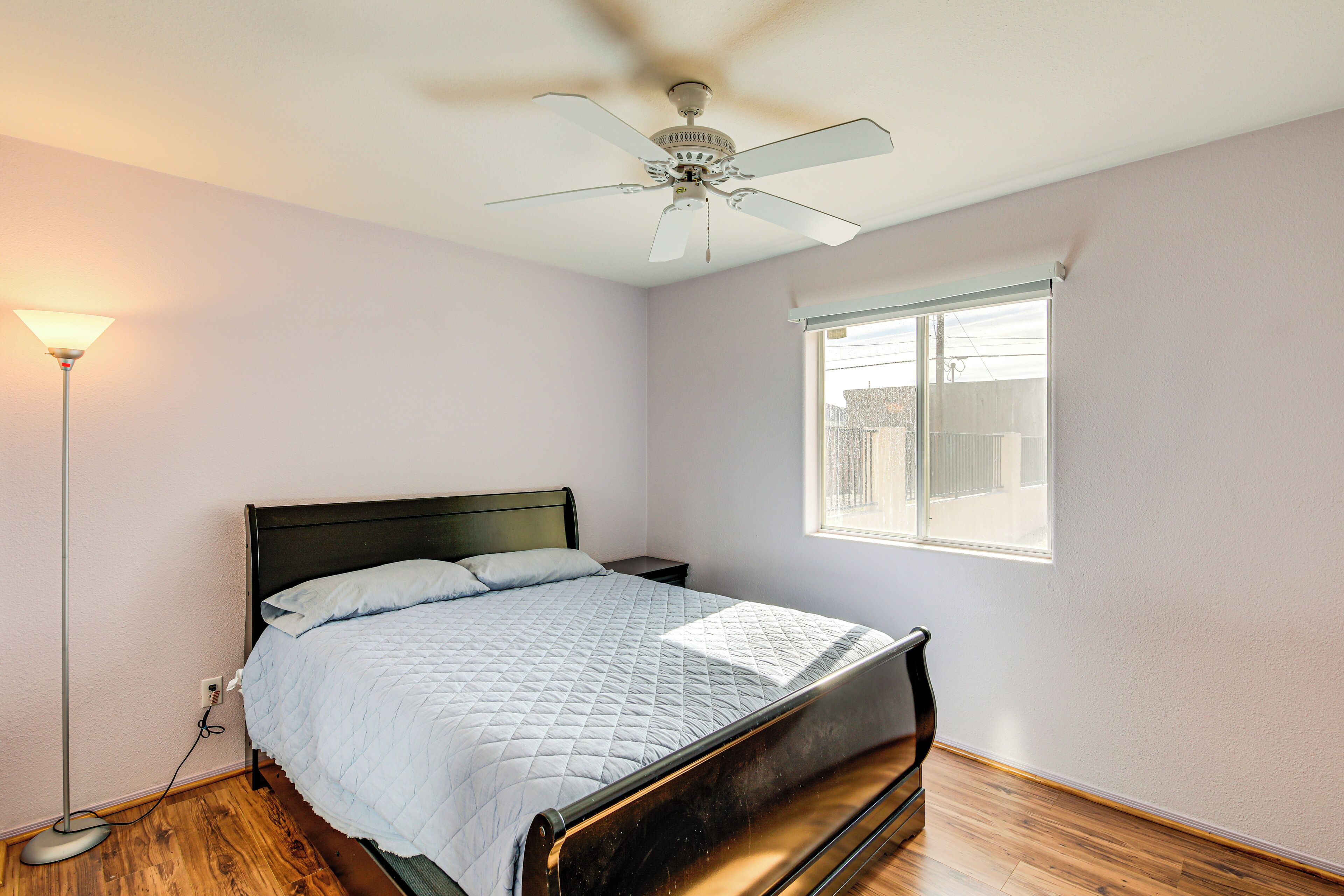 A bedroom with a bed, a ceiling fan, a bedside lamp, and a window.
