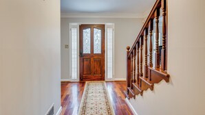 Un pasillo con piso de madera, un tapete estampado, una escalera de madera con barandilla y una puerta doble con paneles de vidrio.