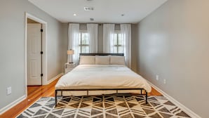 Un dormitorio con cama, alfombra estampada, mesita de noche y ventana con cortinas.