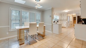 Una cocina moderna con armarios blancos, una isla central y un comedor con mesa y sillas blancas.