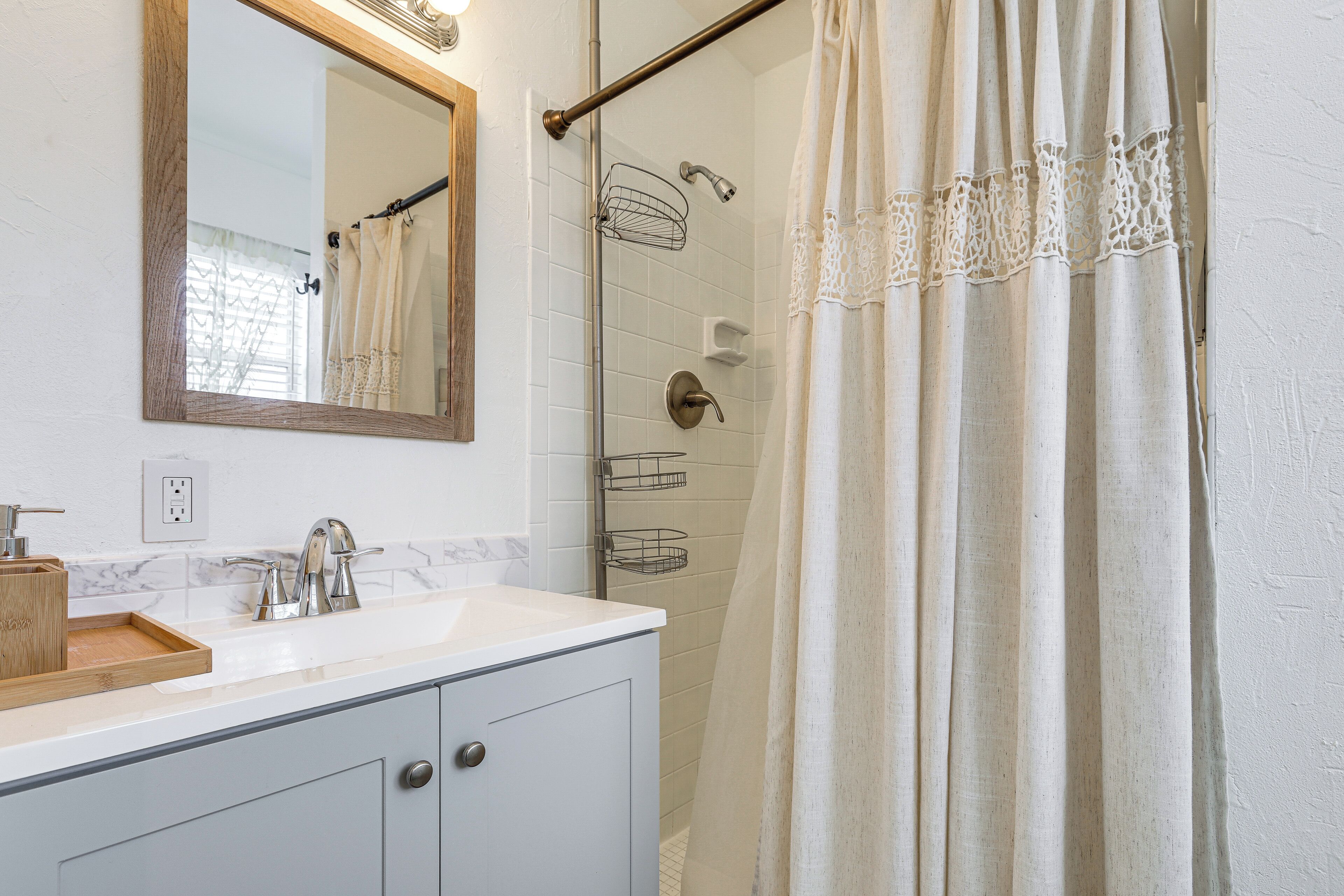 A bathroom with a white sink, a mirror, and a shower area with a curtain.