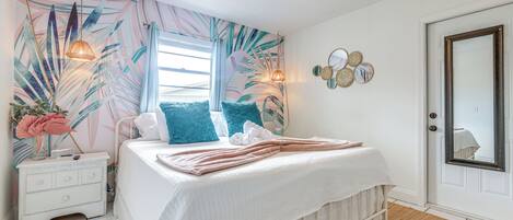A bedroom with a bed, nightstand, and a wall with a tropical leaf pattern.
