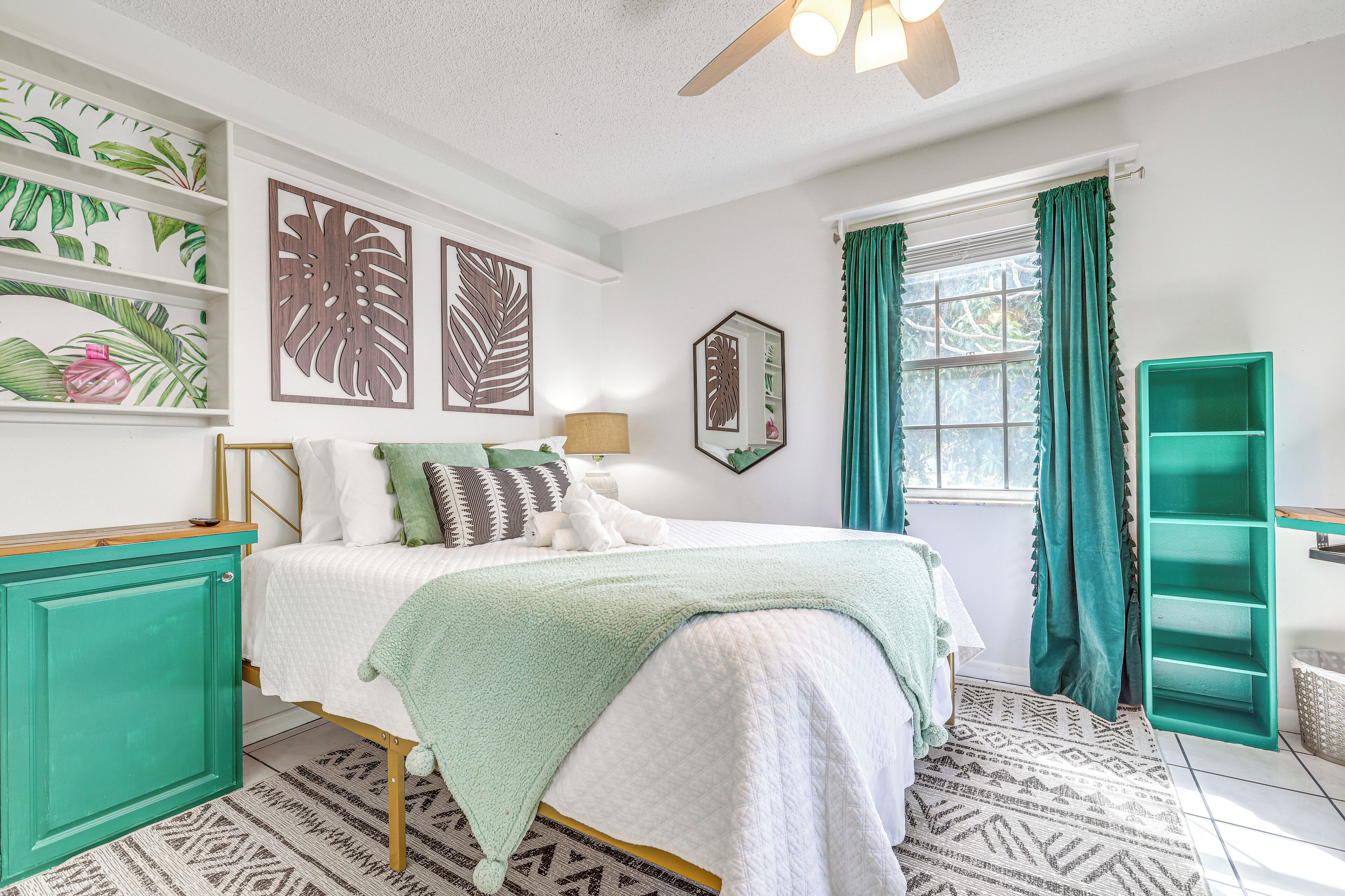 A neatly arranged bedroom with a bed, a teal cabinet, and a window with curtains.