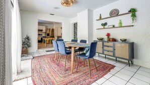 Un coin repas avec une table en bois et des chaises bleues, un tapis à motifs et un meuble avec des étagères adossé au mur.