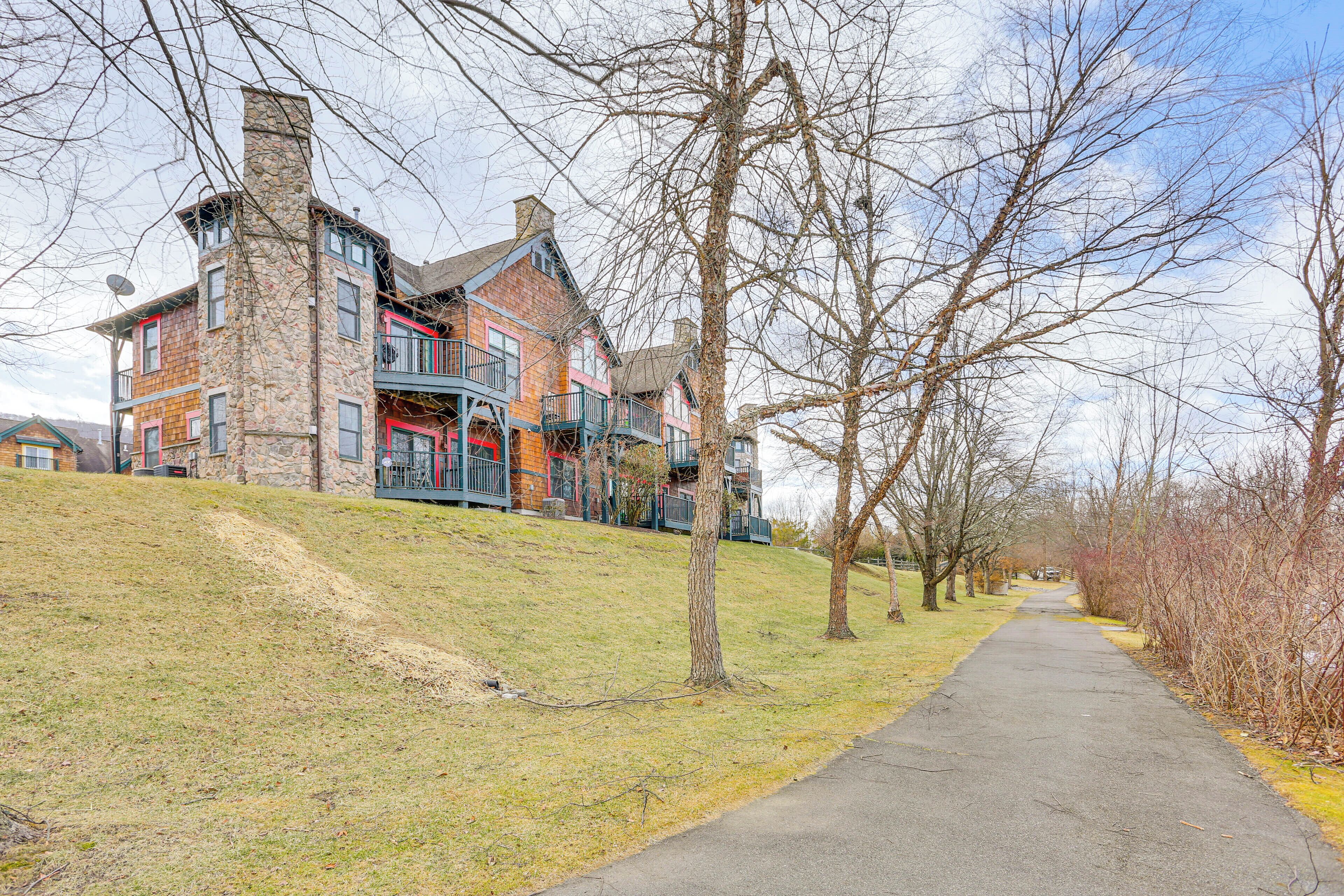 A multi-story building with a stone facade and balconies, located beside a paved walkway with trees.