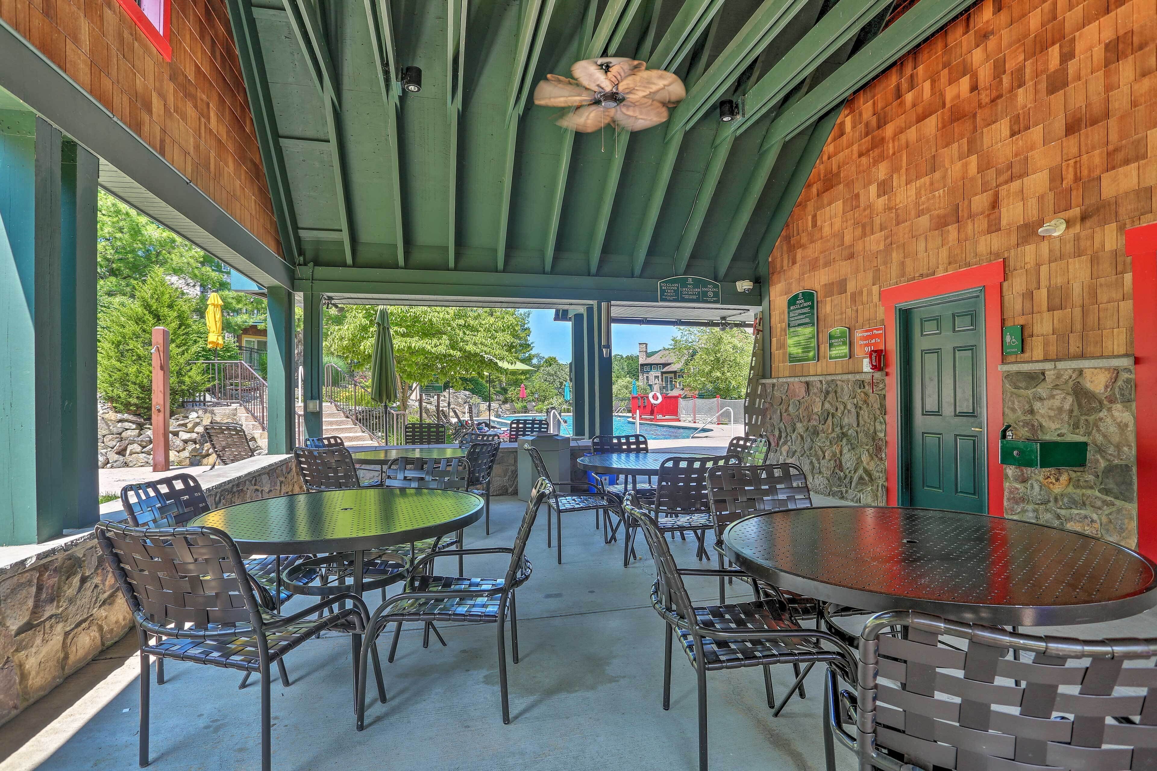 An outdoor patio area with round tables and chairs, a ceiling fan, and a stone wall.