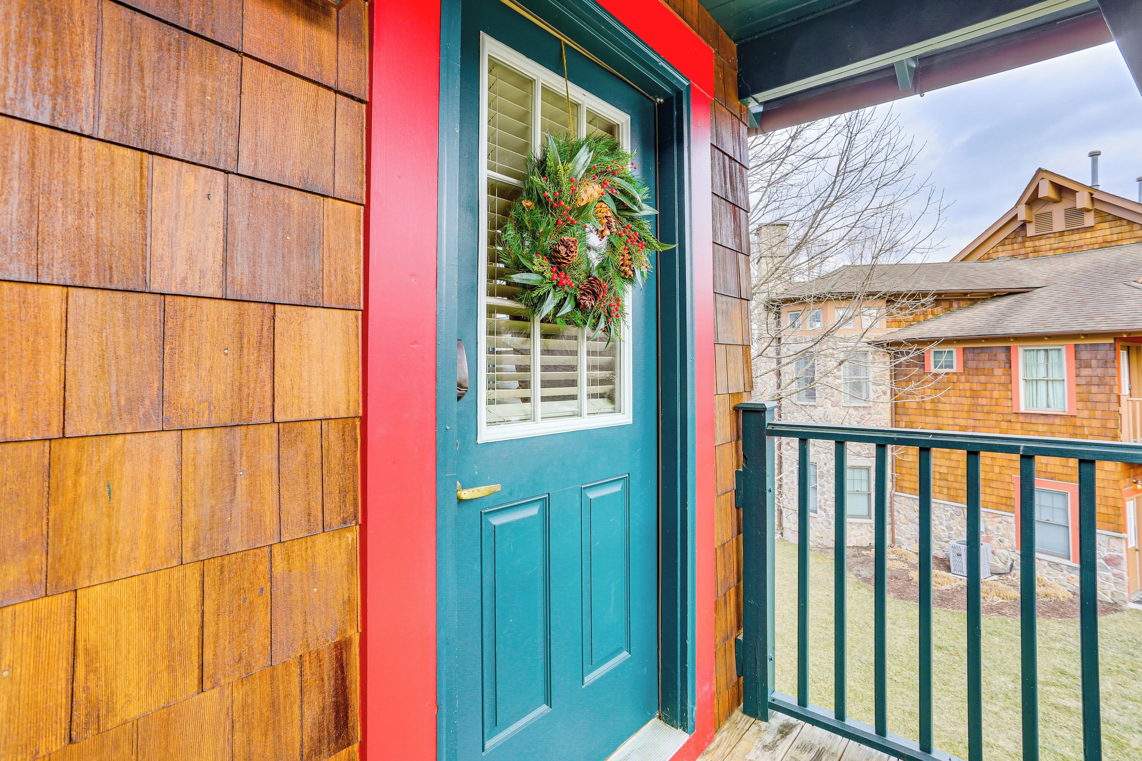 Une maison en bois avec une porte de couleur turquoise et une guirlande accrochée à la fenêtre.