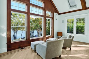 A spacious room with large windows, a wooden ceiling, and a view of trees and water.
