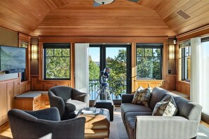 A room with a wooden ceiling, large windows, a telescope, and a television.