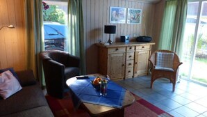 A cozy living room with a brown sofa, a wooden cabinet, a wicker chair, and a coffee table with a blue tablecloth. - Ferienhaus mit Sauna im Ferienpark Mirow (Mirow)