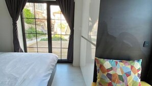 Un dormitorio con cama, almohada colorida, ventana con cortinas y vista al exterior.