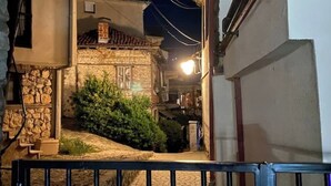 Una calle estrecha con edificios de piedra, un camino empedrado y una barandilla de metal.