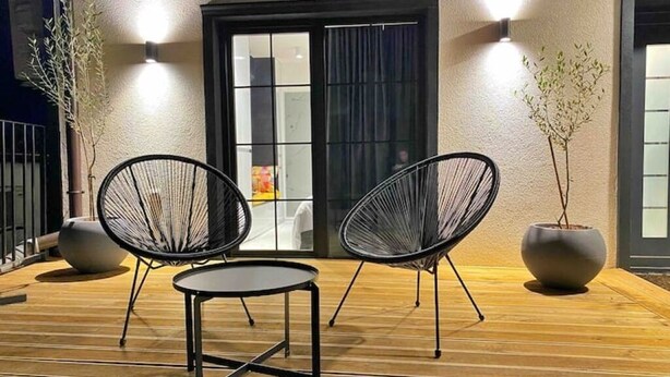 Un área de estar al aire libre con dos sillas de estructura metálica negra y una pequeña mesa redonda sobre un muelle de madera.