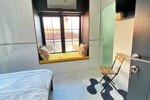 Un dormitorio con cama, un rincón ventana con cojines, una silla y un armario.
