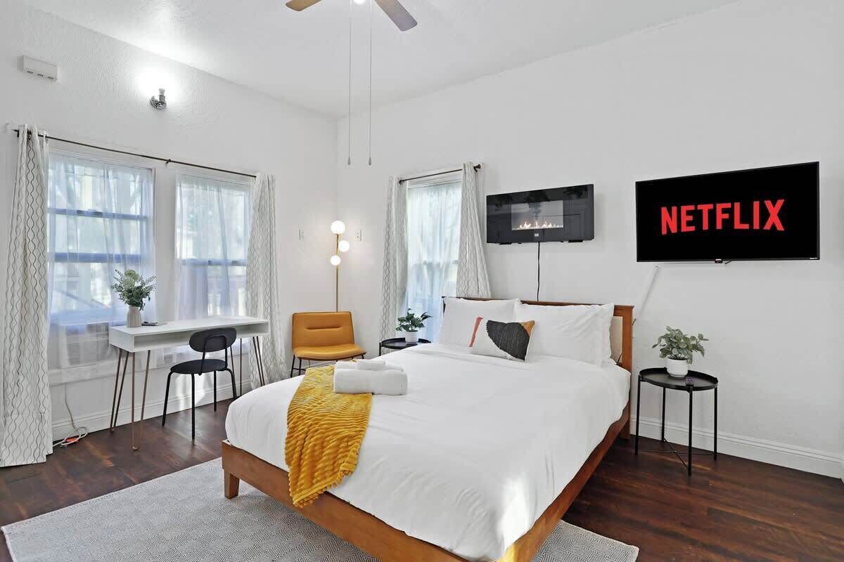 Un dormitorio con cama, escritorio, silla, televisor y una mesita con una planta.