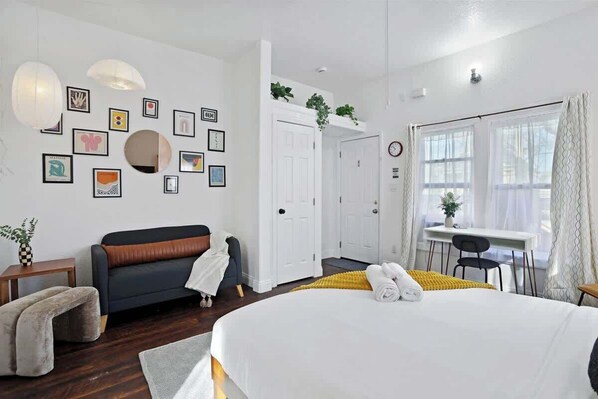 A modern hotel room with a large bed, a sofa, a desk, and a dining area.