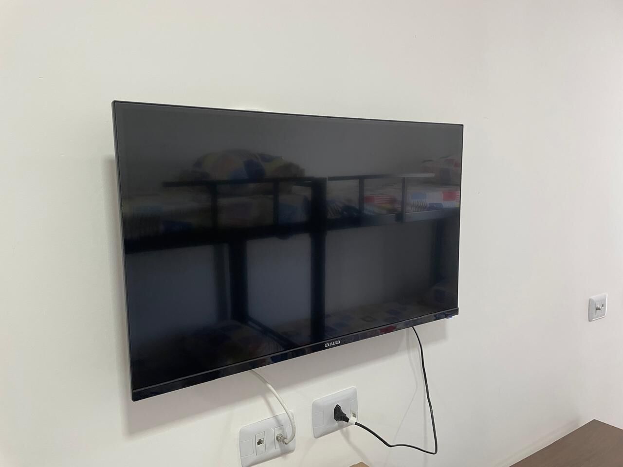 Ein Flachbildfernseher an einer weißen Wand, mit Steckdose und Kabelmanagement.