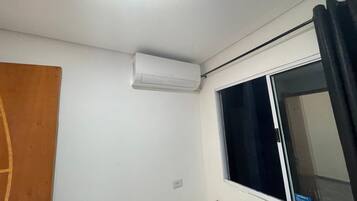 Une petite pièce propre, dotée d’une fenêtre, d’une porte et d’un climatiseur fixé au mur.