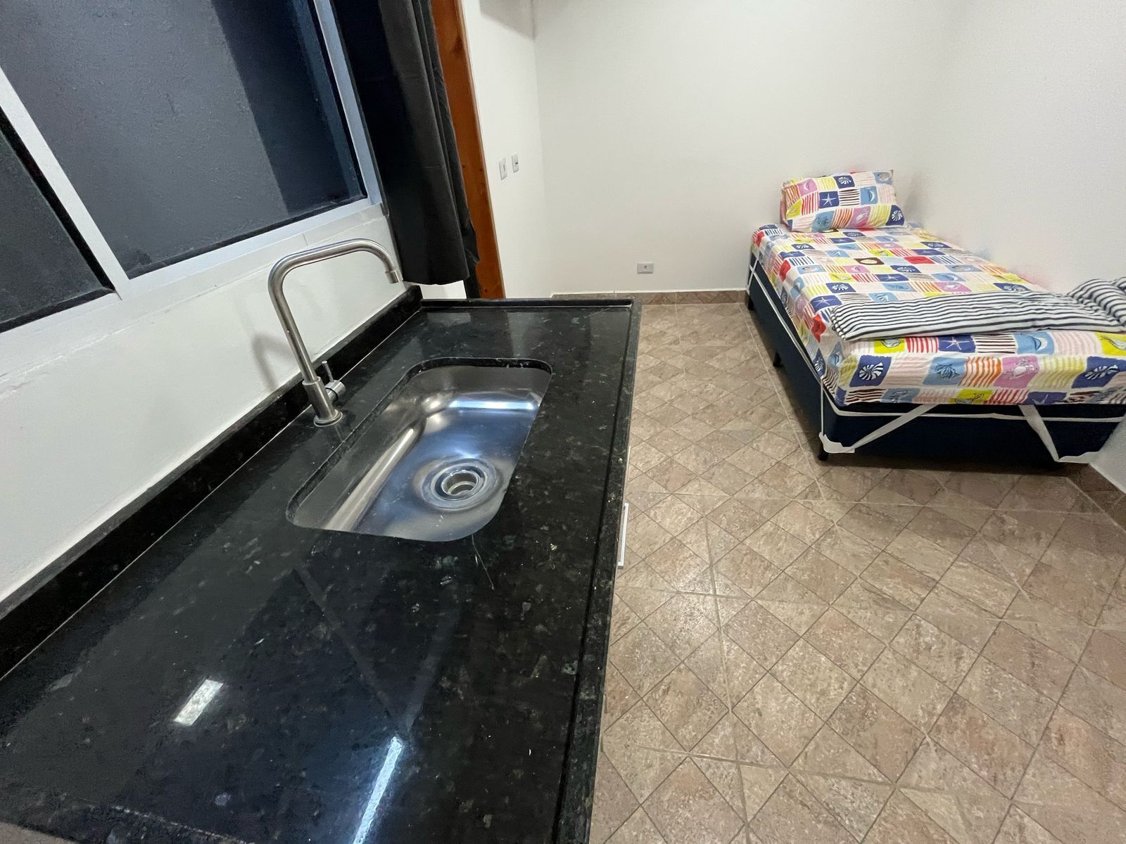 A small room with a black sink, a bed with a colorful quilt, and a tiled floor.