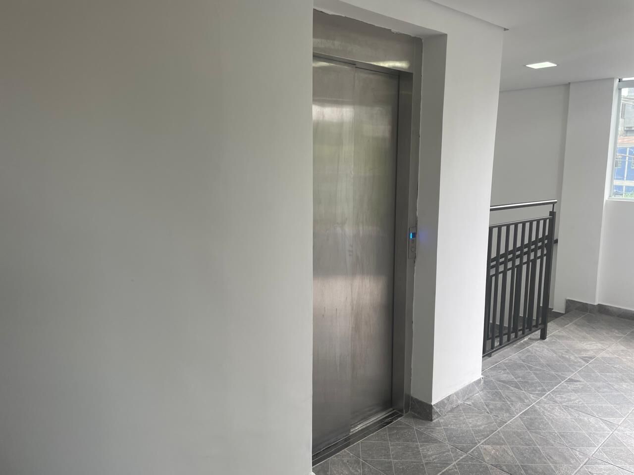 Un ascensor moderno en un pasillo con barandilla metálica y suelo de baldosas.