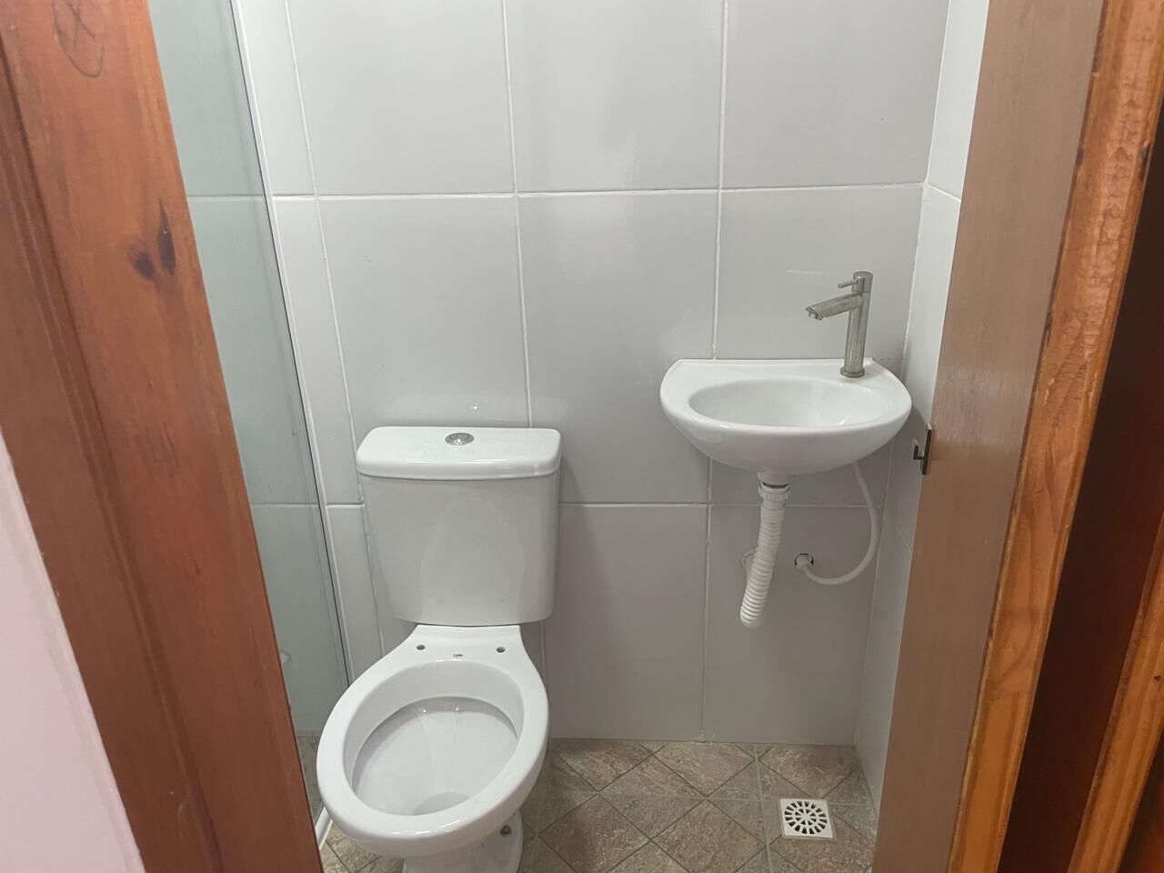 Une petite salle de bain propre, avec des toilettes et un lavabo blancs, des murs carrelés et une porte en bois.