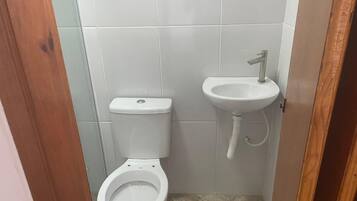 Une petite salle de bain propre, avec des toilettes et un lavabo blancs, des murs carrelés et une porte en bois.