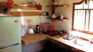 Een kleine keuken met een koelkast, blender, waterkoker en diverse keukengerei op houten planken.