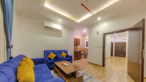 A living room with a blue sofa, a wooden coffee table, and a kitchen in the background. - أحلى الليالي للشقق الفندقية Ahla Al Layali Hotel Apartments (Yanbu)