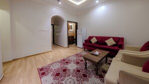 A living room with a red sofa, beige armchairs, a wooden coffee table, and a patterned rug. - أحلى الليالي للشقق الفندقية Ahla Al Layali Hotel Apartments (Yanbu)