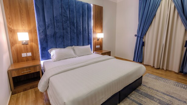 A neatly arranged bedroom with a large bed, wooden nightstands, and a blue curtain. - أحلى الليالي للشقق الفندقية Ahla Al Layali Hotel Apartments (Yanbu)