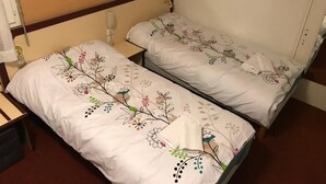 Two single beds with floral bedding, a bedside telephone, and a mirror on the wall. - HOTEL MYOSOTIS (Lourdes)