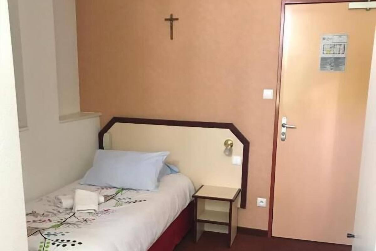 Une chambre avec un lit simple, une tête de lit en bois, une table de chevet et une porte avec une pancarte.