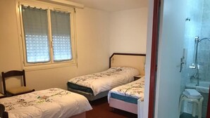 A bedroom with two single beds, a window with curtains, a chair, and a bathroom with a shower and sink. - HOTEL MYOSOTIS (Lourdes)