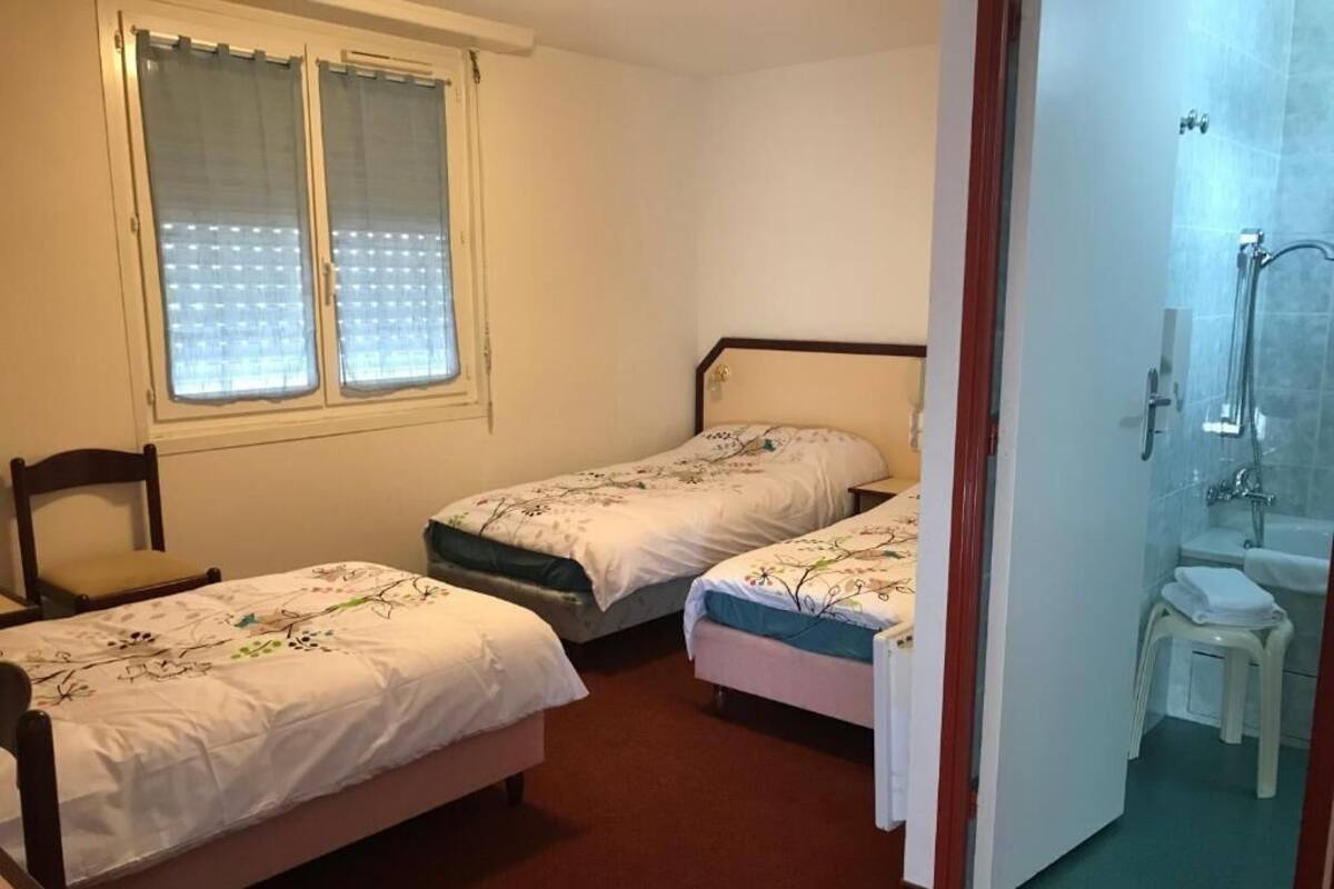 Une chambre avec deux lits simples, une fenêtre avec des rideaux, une chaise et une salle de bain avec une douche et un lavabo.