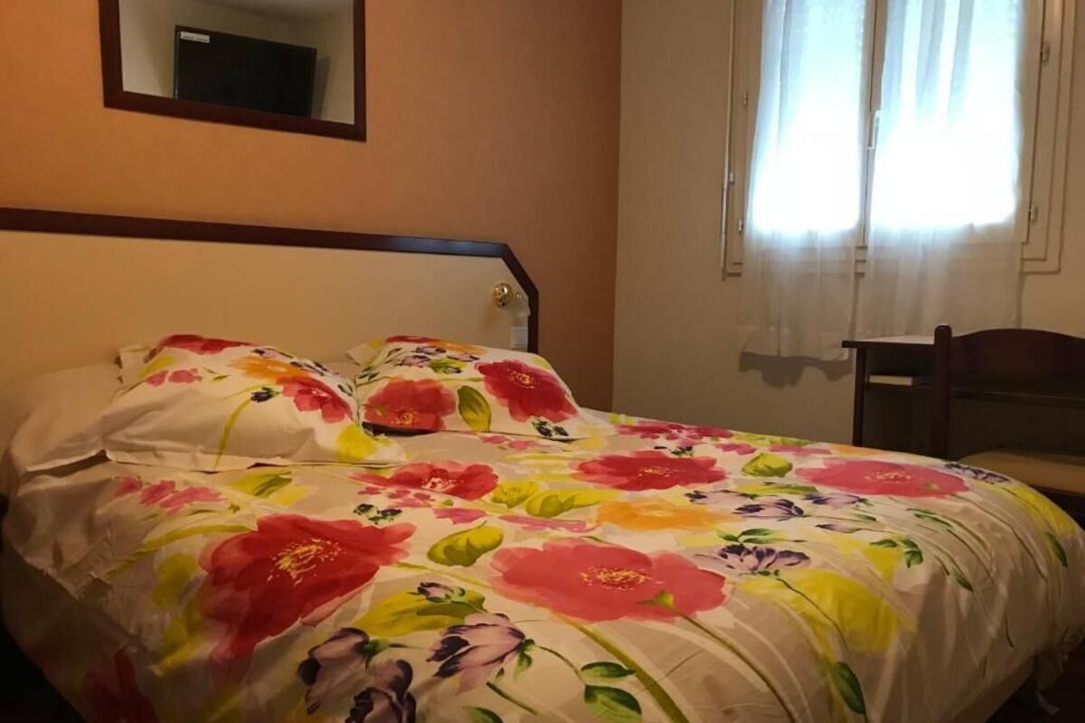 Une chambre à coucher avec une couvre-lit à motifs floraux, une tête de lit en bois, une table de chevet et une chaise.