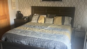 A bedroom with a bed, a ceiling fan, a nightstand, a wall clock, and a decorative sign.