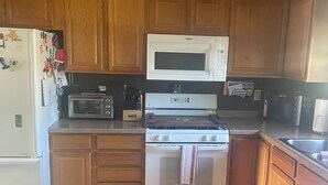 A kitchen with wooden cabinets, a white refrigerator, a microwave, a stove, and a sink.