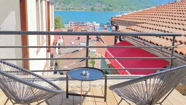 Un balcon avec deux chaises en métal et une petite table, d’où l’on peut admirer un plan d’eau et des bâtiments aux toits rouges.