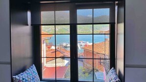 Une pièce dotée d’une grande fenêtre donnant sur une ville côtière et la mer.