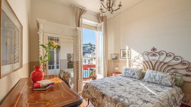 Ein Schlafzimmer mit Bett, Schreibtisch, Blumen in einer Vase und Blick ins Freie.