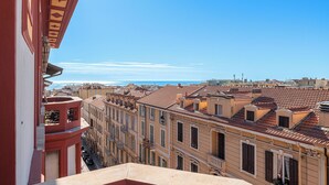 Blick auf eine Küstenstadt mit Gebäuden mit Terrakotta-Dächern, einem klaren blauen Himmel und einer entfernten Meeransicht.
