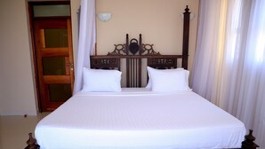 Un letto rifatto con cura, con testiera in legno, biancheria bianca e una porta con pannello in vetro.