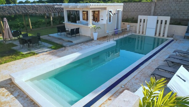 Una piscina rettangolare con solarium bianco e un piccolo edificio con balcone.