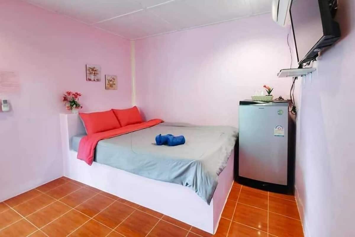 A small, single-bed room with a pink wall, a white bed, and a small refrigerator.