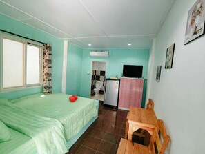Una habitación con cama, una mesa de madera, una pequeña cocina y un baño a la vista a través de una puerta abierta.