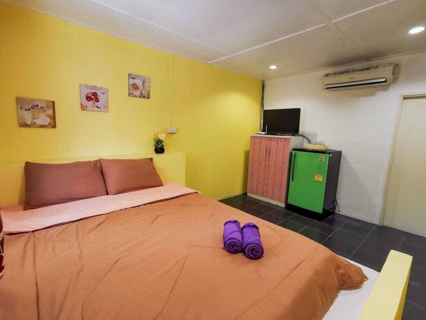A hotel room with a bed, a small refrigerator, an air conditioner, and a television on a cabinet.
